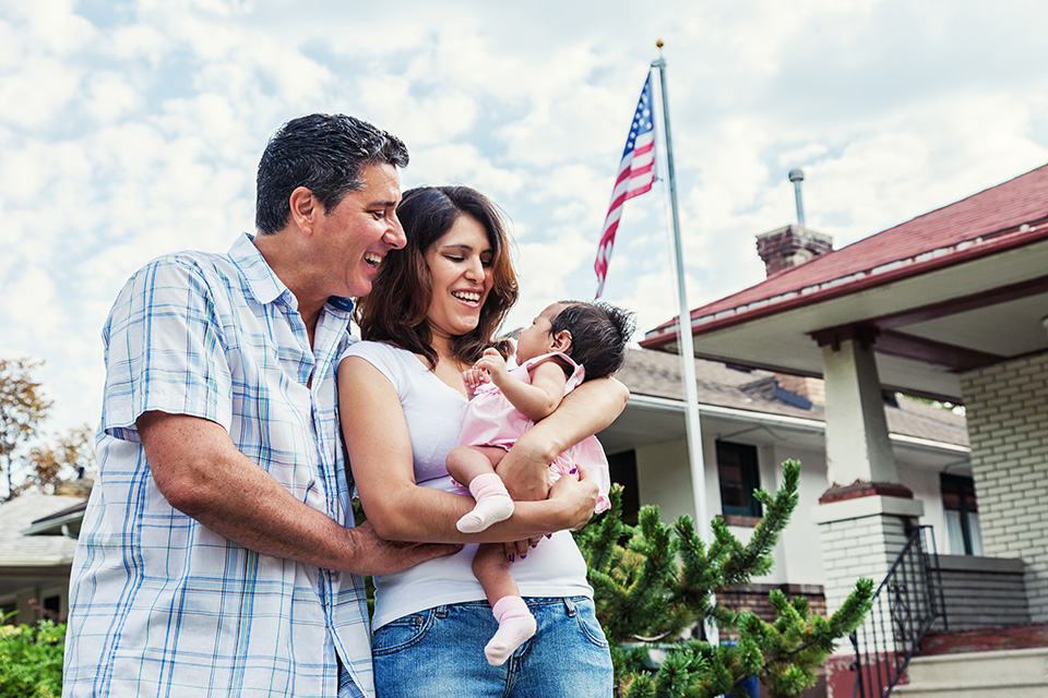 Photo of a new parents standing in their front yard with their new baby girl on a warm summer day.